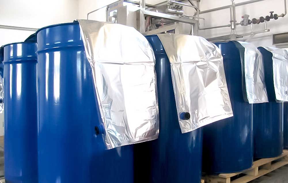 Metallized flexible bag liners positioned inside blue industrial drums